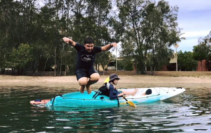 Child jumping off Viking Espri kayak while another paddles near shore