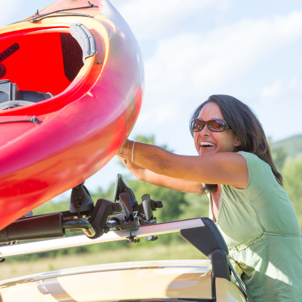 Woman carrying a red tandem kayak toward the water