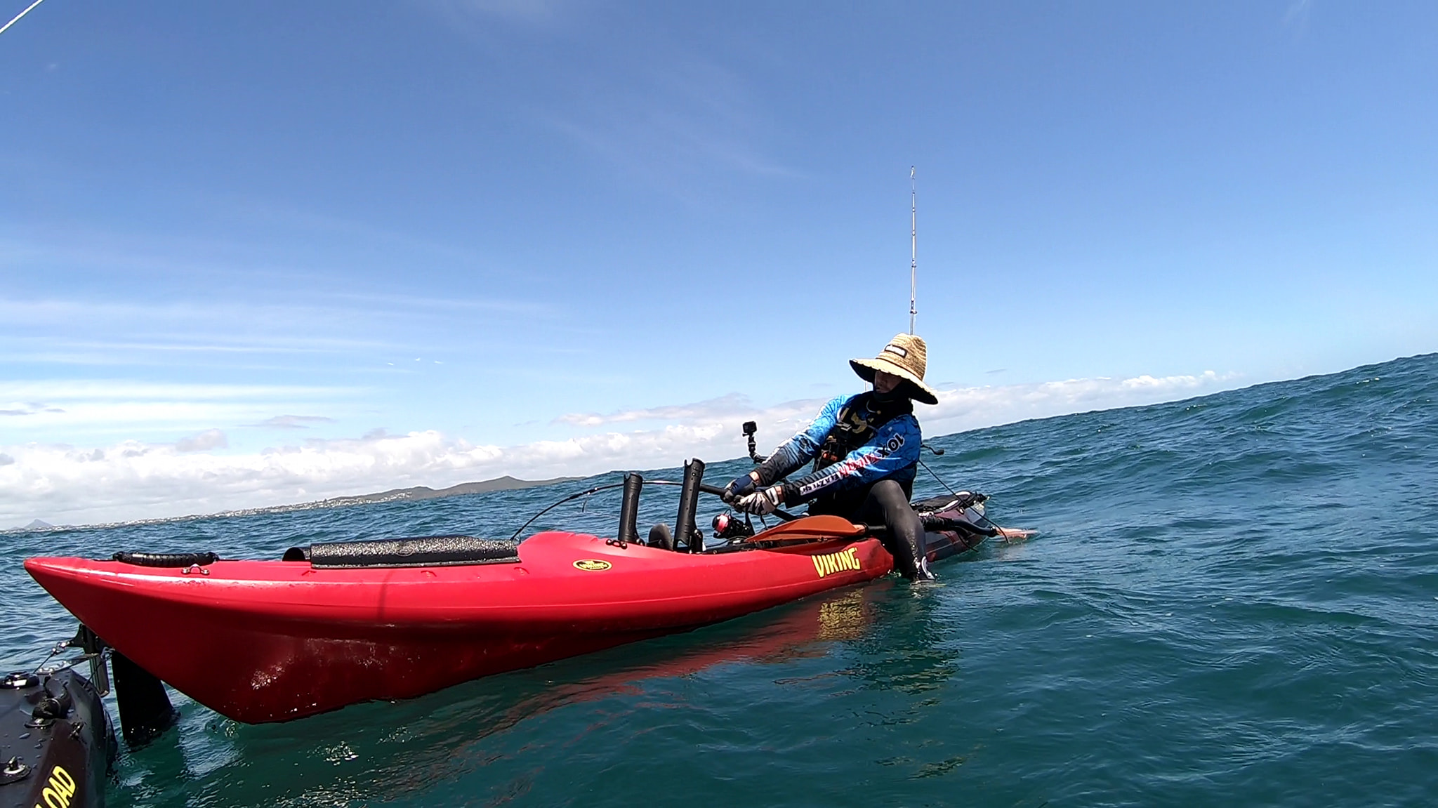 Jason fishing offshore on a red Viking Profish Reload kayak, wearing a straw hat and blue paddle shirt, with fishing rod bent under tension.