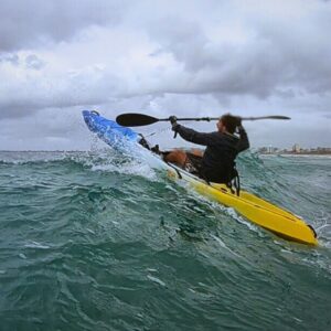 Kayak launching off a wave with urban skyline in the background