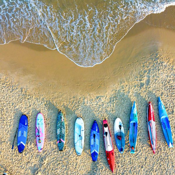 Aerial view of colorful kayaks and sups lined up on the beach by the shoreline.